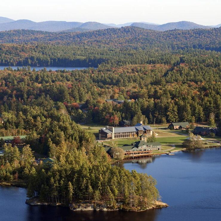 Aerial view of the Paul Smith's College campus with a lake in the foreground and mountains in the distance